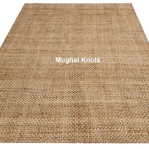 K&ouml;nnte beinhalten: Ein Naturfaser-Teppich in hellbrauner Farbe. Der Teppich ist mit einer dichten, gleichm&auml;&szlig;igen Webart gewebt und hat eine leicht strukturierte Oberfl&auml;che. Der Teppich wird von Mughal Knots hergestellt.