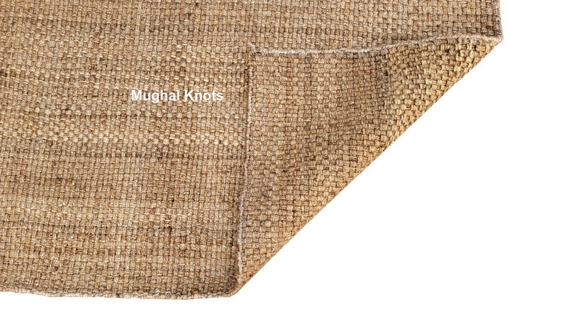 K&ouml;nnte beinhalten: Nahaufnahme eines Naturfaser-Teppichs mit gewebter Textur. Der Teppich ist umgeklappt, wodurch die Unterseite sichtbar wird. Der Text "Mughal Knots" ist auf dem Teppich zu sehen.