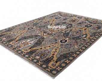 May include: A rectangular area rug with an intricate pattern in shades of gray, beige, and blue. The rug features a central design with floral and geometric elements, framed by a dark border with repeating motifs. The rug has a fringe on the edges.
