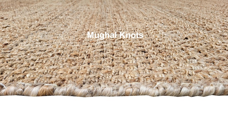 K&ouml;nnte beinhalten: Nahaufnahme eines Naturfaser-Teppichs mit gewebter Textur. Der Teppich hat eine hellbraune Farbe und einen ausgefransten Rand. Der Text "Mughal Knots" ist im Bild sichtbar.