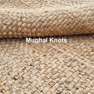 K&ouml;nnte beinhalten: Nahaufnahme eines Naturfaser-Teppichs mit einem gewebten Muster. Der Teppich ist aus Jute und hat eine hellbraune Farbe. Der Text "Mughal Knots" ist im Bild sichtbar.