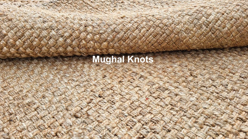 K&ouml;nnte beinhalten: Nahaufnahme eines Naturfaser-Teppichs mit einem gewebten Muster. Der Teppich ist aus Jute und hat eine hellbraune Farbe. Der Text "Mughal Knots" ist im Bild sichtbar.