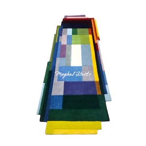 May include: A colorful abstract rug with a geometric pattern in shades of blue, green, yellow, and purple. The rug is made of hand-knotted wool and has a fringe border. The text "Mughal Knots" is visible in the center of the rug.