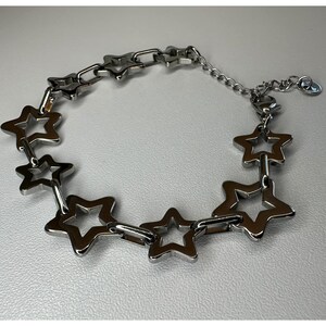 Peut inclure: Un bracelet argenté orné d'une série d'étoiles ajourées reliées entre elles. Le bracelet est doté d'une chaîne d'extension pour un ajustement sur mesure et d'un petit charme. Les étoiles sont espacées de manière uniforme.