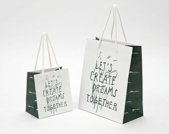 May include: Two white paper shopping bags with green accents. The larger bag has the text "Let's Create Dreams Together" printed on the front. The smaller bag has the same text printed on the front.