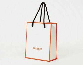 May include: A white shopping bag with an orange border and black handles. The bag has the text "HARBORS" printed on the front.