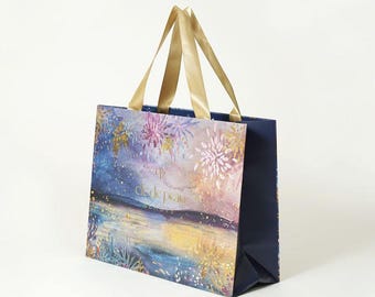 Puede incluir: Una bolsa de regalo azul marino con asas doradas. La bolsa presenta un diseño artístico y colorido de fuegos artificiales sobre una masa de agua. El texto "Clé de Peau Beauté" está impreso en la parte delantera de la bolsa.
