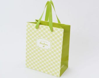 Puede incluir: Una bolsa de regalo verde con un patrón de cuadros blanco y verde claro. La bolsa tiene asas verdes y la palabra "Bonbons" en una etiqueta decorativa en la parte delantera.