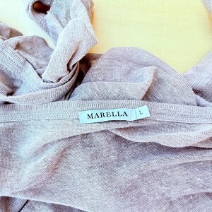 May include: A light mauve, semi-sheer knit garment featuring a white fabric label stitched at the neckline. The label displays the text MARELLA in black capital letters, followed by the letter L to indicate size. The fabric has a visible texture.