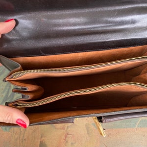 May include: A brown leather briefcase with two zippered compartments and a smaller pocket on the front. The interior is lined with a brown fabric.