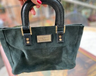 May include: A dark green suede handbag with black leather handles and gold hardware. The bag has a gold metal plate with the text "Who's Who" on it.