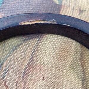 May include: Close-up of a black leather ring with a small tear in the leather.