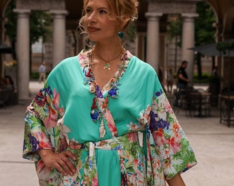 Könnte beinhalten: Eine Frau trägt einen türkisfarbenen Kimono mit Blumenmuster. Sie trägt eine mehrfarbige Halskette mit einer goldenen Kette und ein goldenes Armband.