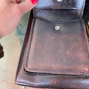 May include: A brown leather briefcase with a gold metal lock and a small pocket on the front. The briefcase is open and the inside is lined with a brown fabric.