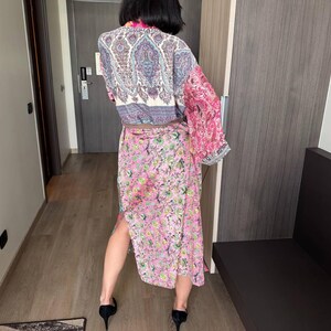May include: A long, flowing pink and blue patterned robe with a paisley design. The robe is tied at the waist with a matching belt.