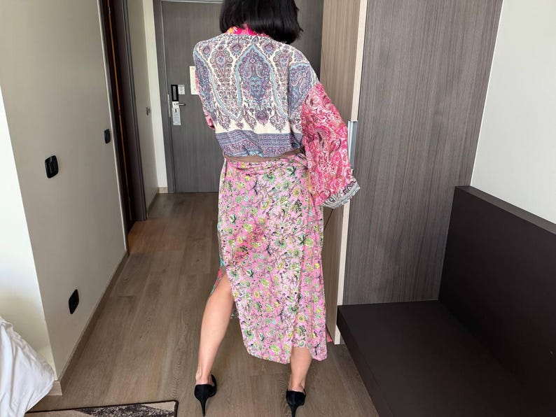 May include: A long, flowing pink and blue patterned robe with a paisley design. The robe is tied at the waist with a matching belt.