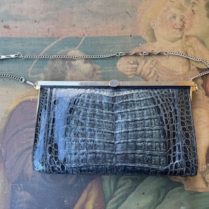 Puede incluir: Un bolso de mano negro con estampado de cocodrilo, con una cadena de plata y un cierre de plata.
