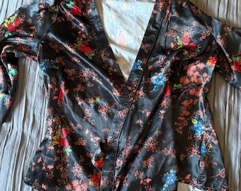 May include: A black satin wrap top with a floral print in shades of pink, red, blue, and green. The top has a V-neckline and long sleeves.