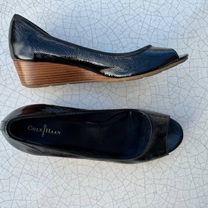 May include: A pair of black leather peep-toe wedge heels with a wooden platform. The shoes are labelled "Cole Haan".