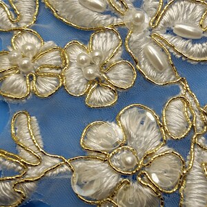 May include: White floral lace trim with gold beading and pearl accents on a light blue background.
