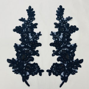 May include: Two navy blue floral lace appliques with beaded details. The appliques are symmetrical and feature a delicate floral design with intricate beading.