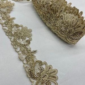 May include: Gold beaded lace trim with a delicate floral pattern. The trim is rolled up and shows the intricate details of the design.