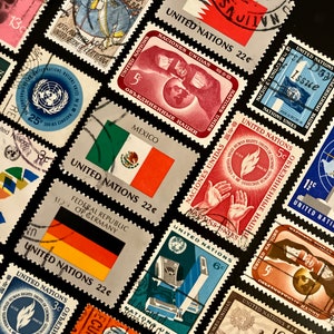 Op de afbeelding: Een verzameling vintage postzegels van de Verenigde Naties. De postzegels tonen diverse ontwerpen, waaronder vlaggen en illustraties, met tekst in meerdere talen. Kleuren zijn rood, blauw, groen en oranje. Op een zwarte achtergrond.