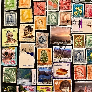 Op de afbeelding: Een verzameling vintage Nieuw-Zeelandse postzegels met verschillende ontwerpen, waaronder landschappen, portretten en flora en fauna. De postzegels zijn in rijen gerangschikt op een donkere achtergrond.