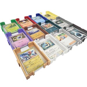 May include: A multi-colored card organizer with several compartments, each holding trading cards. The compartments are in various colors, including green, red, purple, and white. The cards feature colorful illustrations and text.
