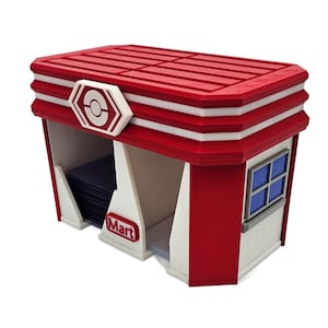 Op de afbeelding: Een rood-witte opbergdoos met een rood dak, witte strepen en een wit embleem. De doos heeft een raam met blauwe ruiten en het woord "Mart" op de voorkant. De doos is ontworpen om kaarten in op te bergen.