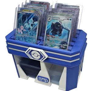 May include: A blue and white Pokémon card display case with multiple trading cards visible. The case has a hexagonal logo and the word "Mart" on the front. The cards are in protective sleeves.