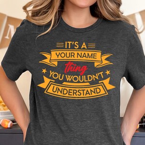 Puede incluir: Una camiseta gris oscura con un gr&aacute;fico amarillo y rojo que dice "Es una cosa de [Tu nombre] que no entender&iacute;as."