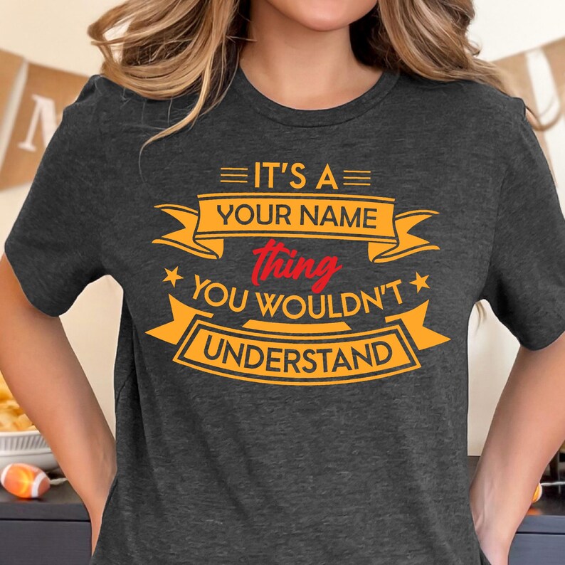 Puede incluir: Una camiseta gris oscura con un gr&aacute;fico amarillo y rojo que dice "Es una cosa de [Tu nombre] que no entender&iacute;as."