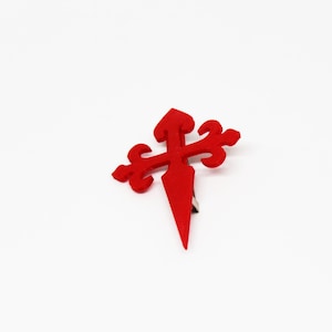 May include: A red felt cross with a pointed tip, a traditional symbol of pilgrimage.