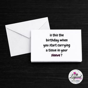 May include: A white greeting card with the text "is this the birthday when you start carrying a tissue in your sleeve?" is next to a white envelope. The card has a black and purple logo in the bottom right corner.