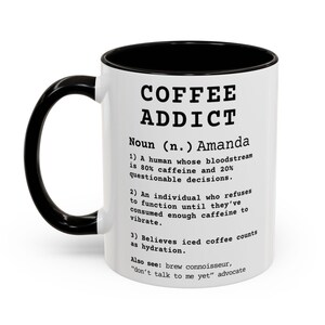 May include: White ceramic coffee mug with a black interior and handle. The mug features the text "COFFEE ADDICT" and a humorous definition, including the phrase "don't talk to me yet".