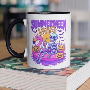 Op de afbeelding: Witte keramische mok met een zwart handvat en rand. De mok heeft een kleurrijke illustratie van een skelet met een zonnebril, drijvend op een flamingo-drijver, met de tekst "Summerween Vibes". Pompoenen en vleermuizen zijn ook inbegrepen.