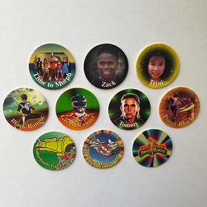 May include: A collection of ten circular cardboard pogs featuring Mighty Morphin Power Rangers imagery. The designs include character portraits of Zack and Trini, action shots of the Black and Green Rangers, Zord illustrations, and the show logo.
