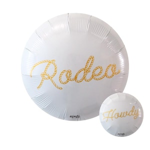 Puede incluir: Dos globos redondos blancos con letras doradas en forma de cuerda. El globo más grande dice "Rodeo" y el globo más pequeño dice "Howdy".
