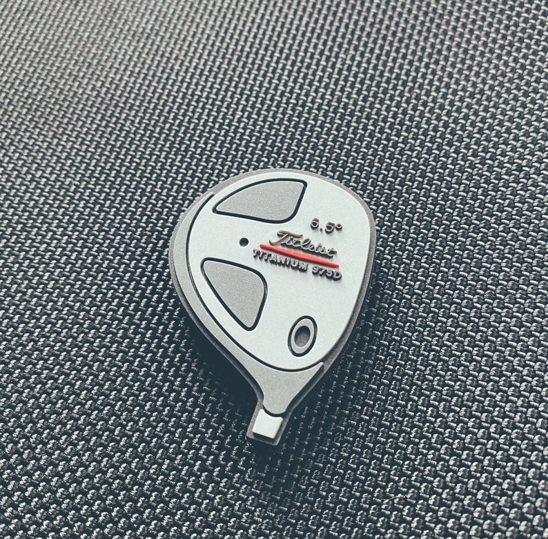 May include: A white golf club head with a silver finish. The club head has a red and white "Titleist" logo and the text "Titanium 975D" and "6.5&deg;".