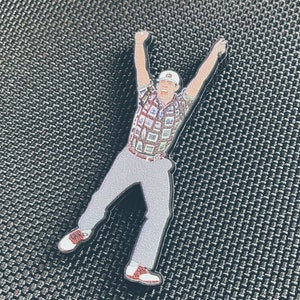 May include: A black and white pin of a person wearing a plaid shirt and grey pants, with their arms raised in the air. The person is wearing a white hat and has a red and white shoe on each foot.