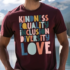 May include: A maroon t-shirt with the words "KINDNESS EQUALITY INCLUSION DIVERSITY LOVE" printed in colorful, stylized letters.