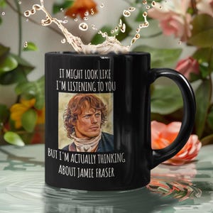 Peut inclure: Mug en céramique noire avec une anse incurvée. Le mug présente le texte "IT MIGHT LOOK LIKE I'M LISTENING TO YOU BUT I'M ACTUALLY THINKING ABOUT JAMIE FRASER" et une image d'un homme.
