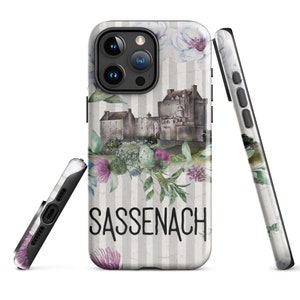 Może przedstawiać: Etui na telefon z akwarelowym wzorem zamku, kwiatów i napisem "Sassenach". Etui jest czarne i ma biało-szare paski.