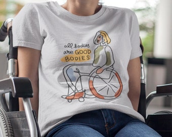 May include: A white short-sleeved t-shirt featuring a line art illustration of a person in a wheelchair. The graphic includes the text "all bodies are GOOD BODIES" in black and yellow, with orange and green accents on the figure and chair.