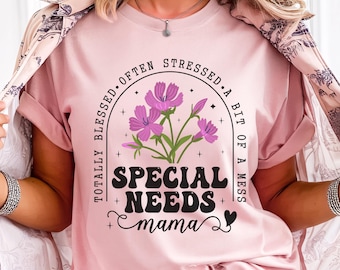 May include: A light pink t-shirt with the words "SPECIAL NEEDS mama" in a black, bold font, with a floral design above the text. The shirt also has the phrases "TOTALLY BLESSED. OFTEN STRESSED. A BIT OF A MESS" in a circular design.