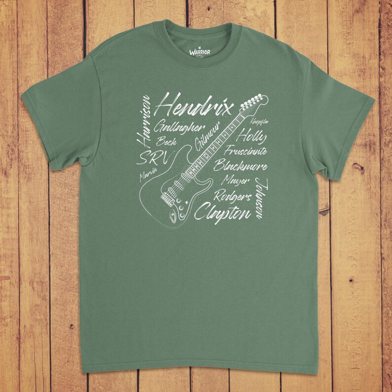 Pode incluir: Uma t-shirt de manga curta verde s&aacute;lvia com um gr&aacute;fico de linhas brancas de uma guitarra el&eacute;trica. O design inclui os nomes Hendrix, Harrison, Gallagher, Beck, SRV, Marvin, Gilmour, Holly, Frusciante, Blackmore, Mayer, Rodgers, Clayton, Knopfler e Johnson.