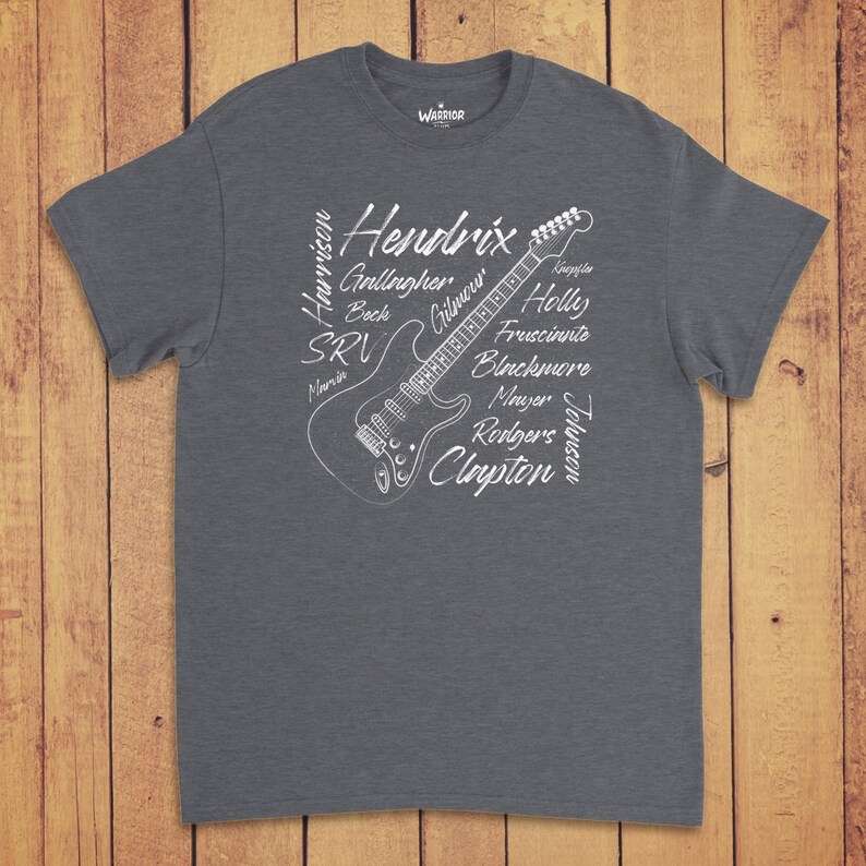 Pode incluir: Uma t-shirt de manga curta em cinzento escuro mesclado com um gr&aacute;fico de linhas brancas de uma guitarra el&eacute;trica. O design incorpora os nomes de guitarristas famosos, incluindo Hendrix, Gilmour, Clapton e outros em letra cursiva.