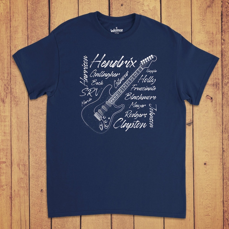 Pode incluir: Uma t-shirt azul-marinho de manga curta com um gr&aacute;fico branco de uma guitarra el&eacute;trica. O design inclui os nomes Hendrix, Gallagher, Beck, SRV, Marvin, Harrison, Knopfler, Holly, Frusciante, Blackmore, Mayer, Rodgers, Johnson e Clapton.