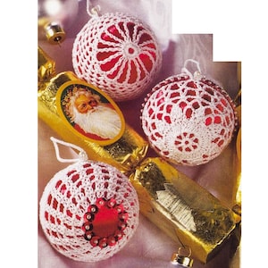 Puede incluir: Tres adornos navideños de crochet blanco con centros rojos. Los adornos están decorados con lentejuelas y están sobre un tubo de papel de regalo dorado.